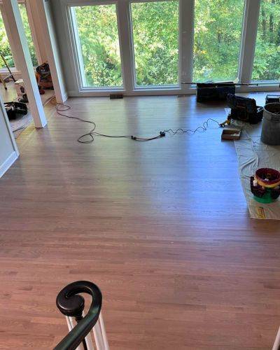 Hardwood floor refinishing in progress in Lenexa, KS, with tools and cables across a bright room.